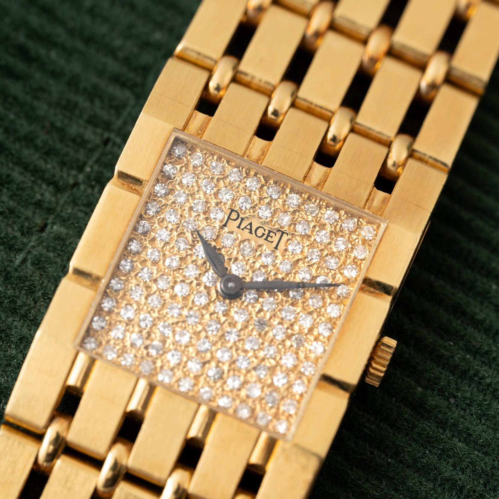 A Piaget Dancer wristwatch with a gold case and diamond-encrusted face displayed against a green textured background.