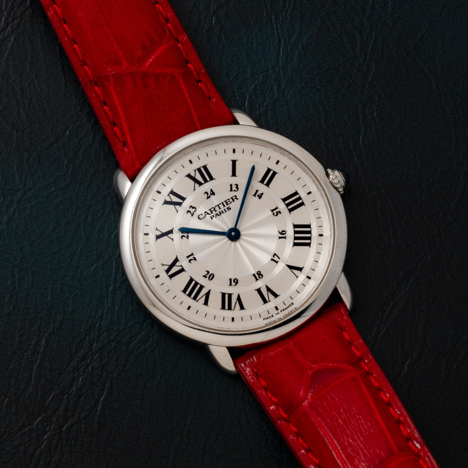 Cartier Ronde Louis CPCP watch with Roman numerals and a red leather strap displayed on a dark textured surface.