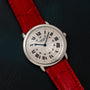 Cartier Ronde Louis CPCP watch with Roman numerals and a red leather strap displayed on a dark textured surface.