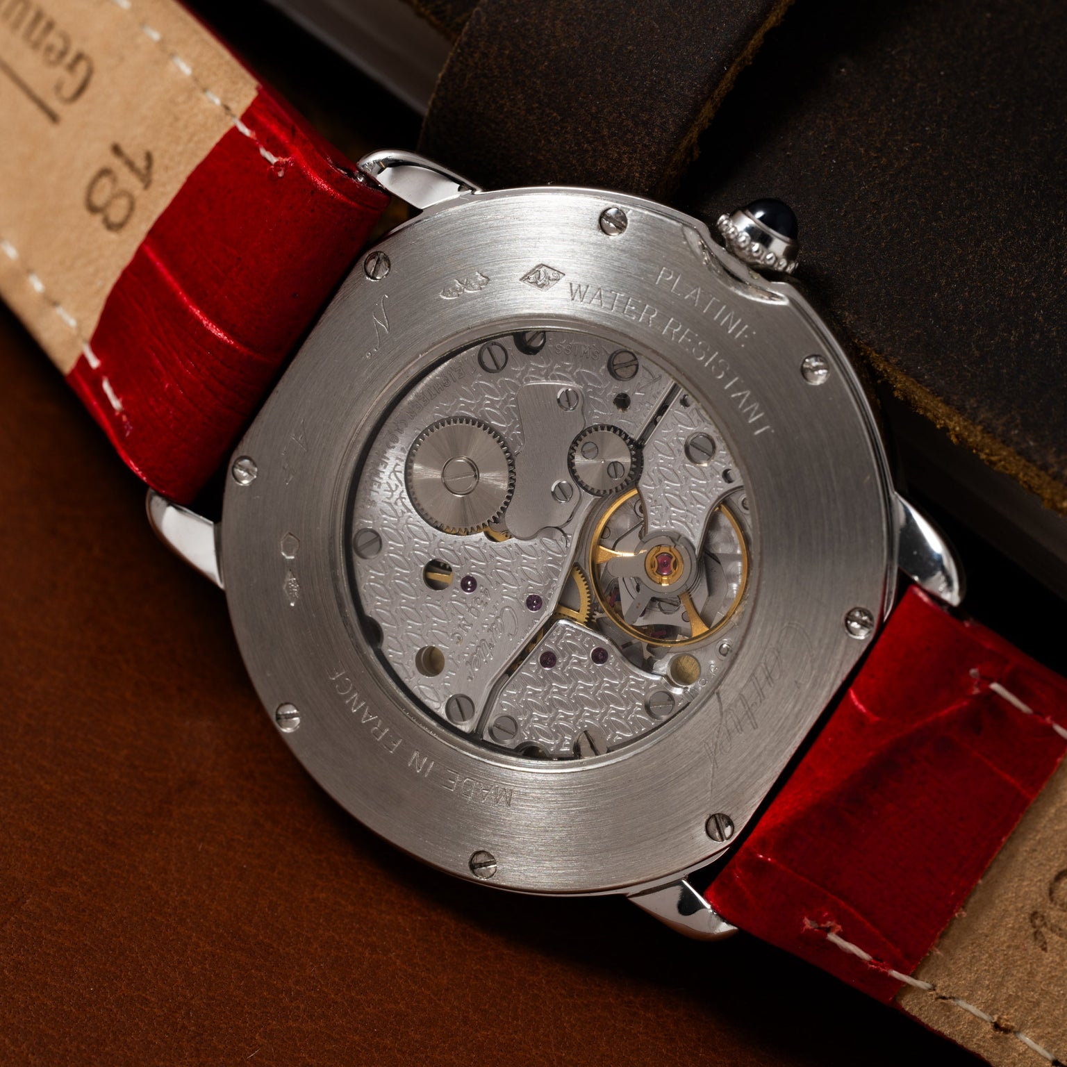 Close-up of the Cartier Ronde Louis CPCP watch, featuring an exposed mechanical movement, visible gears, and a red leather strap.