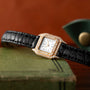 A Cartier Panthère square wristwatch, adorned with diamonds and featuring a black leather strap, rests atop a green book.
