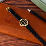 A Piaget Polo Onyx gold watch with a black strap rests on a brown leather notebook beside a black pen.