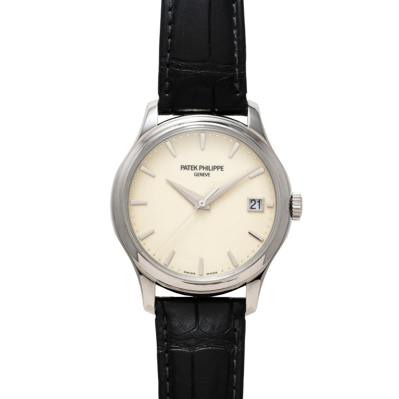 Patek Philippe Calatrava: silver wristwatch with black leather strap, cream dial, and date window at 3 o’clock.