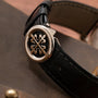 Close-up of a Patek Philippe Calatrava black leather watch strap with a round silver clasp featuring an ornate design.