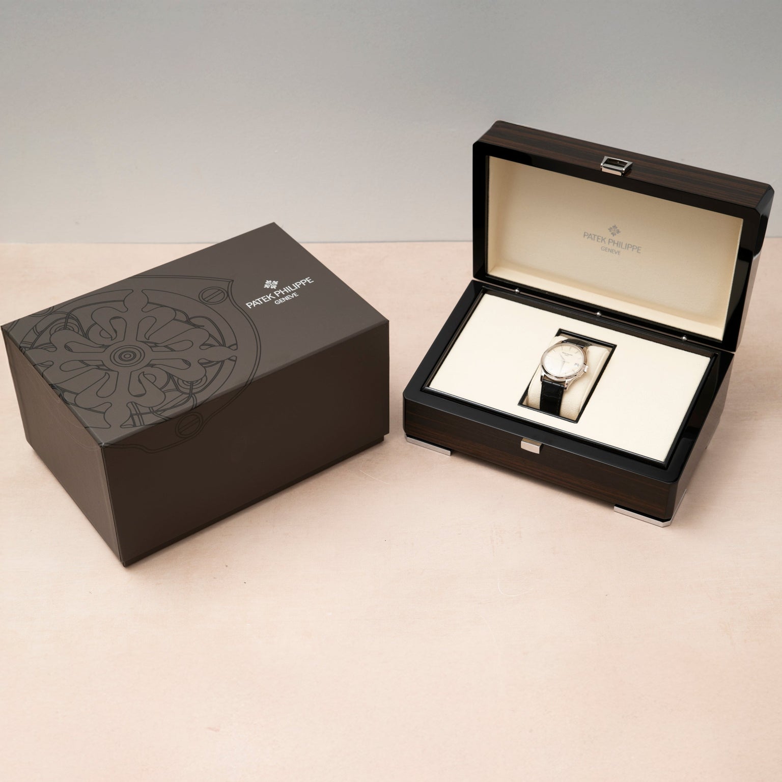 A Patek Philippe Calatrava luxury watch displayed in an open branded box next to its closed packaging on a light surface.