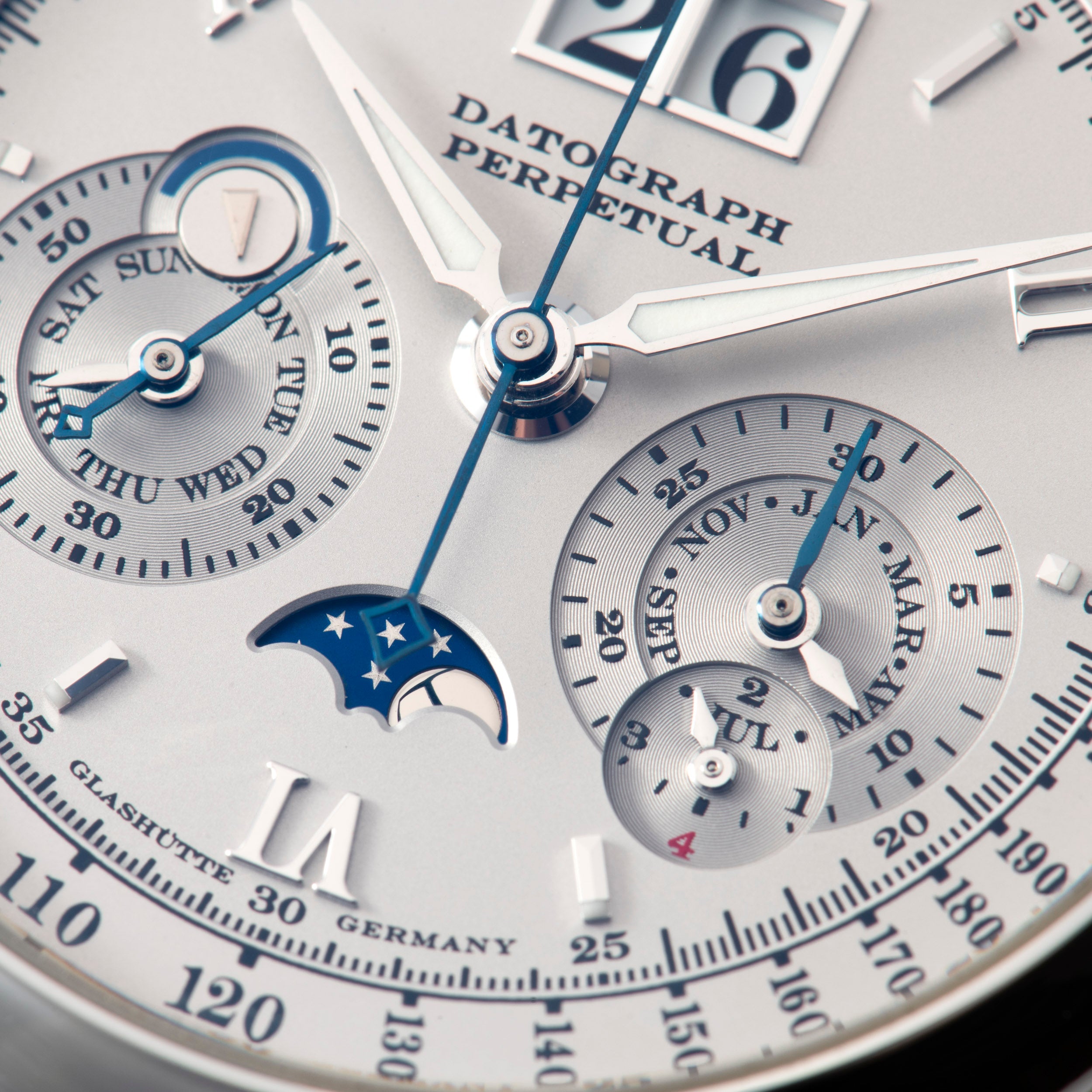Close-up of the Lange & Sohne Datograph Perpetual Calendar watch face featuring multiple dials, blue and silver hands, and a moon phase display.