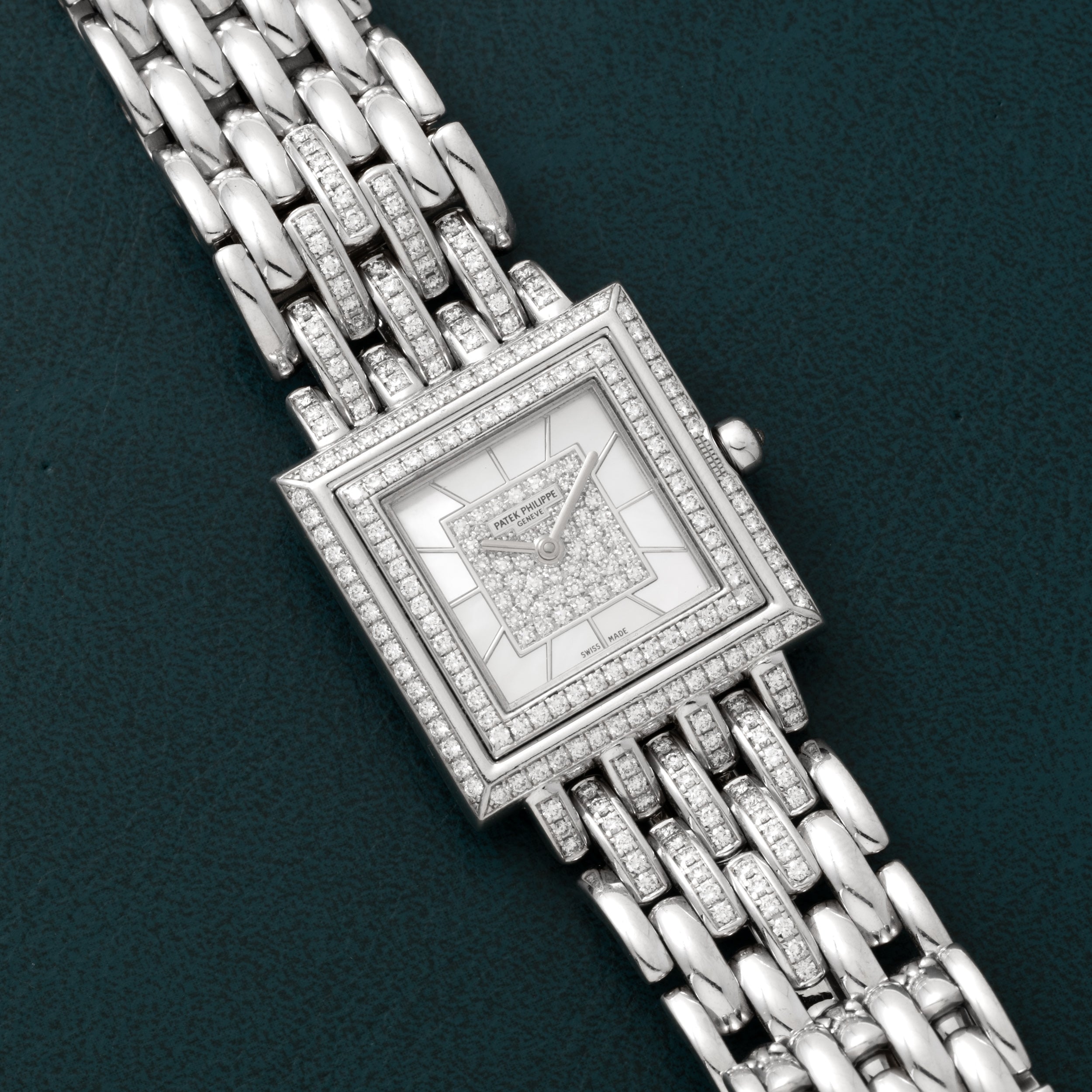 The Patek Philippe Gondolo square wristwatch, adorned with diamonds and a silver metal band, displayed on a dark green background.