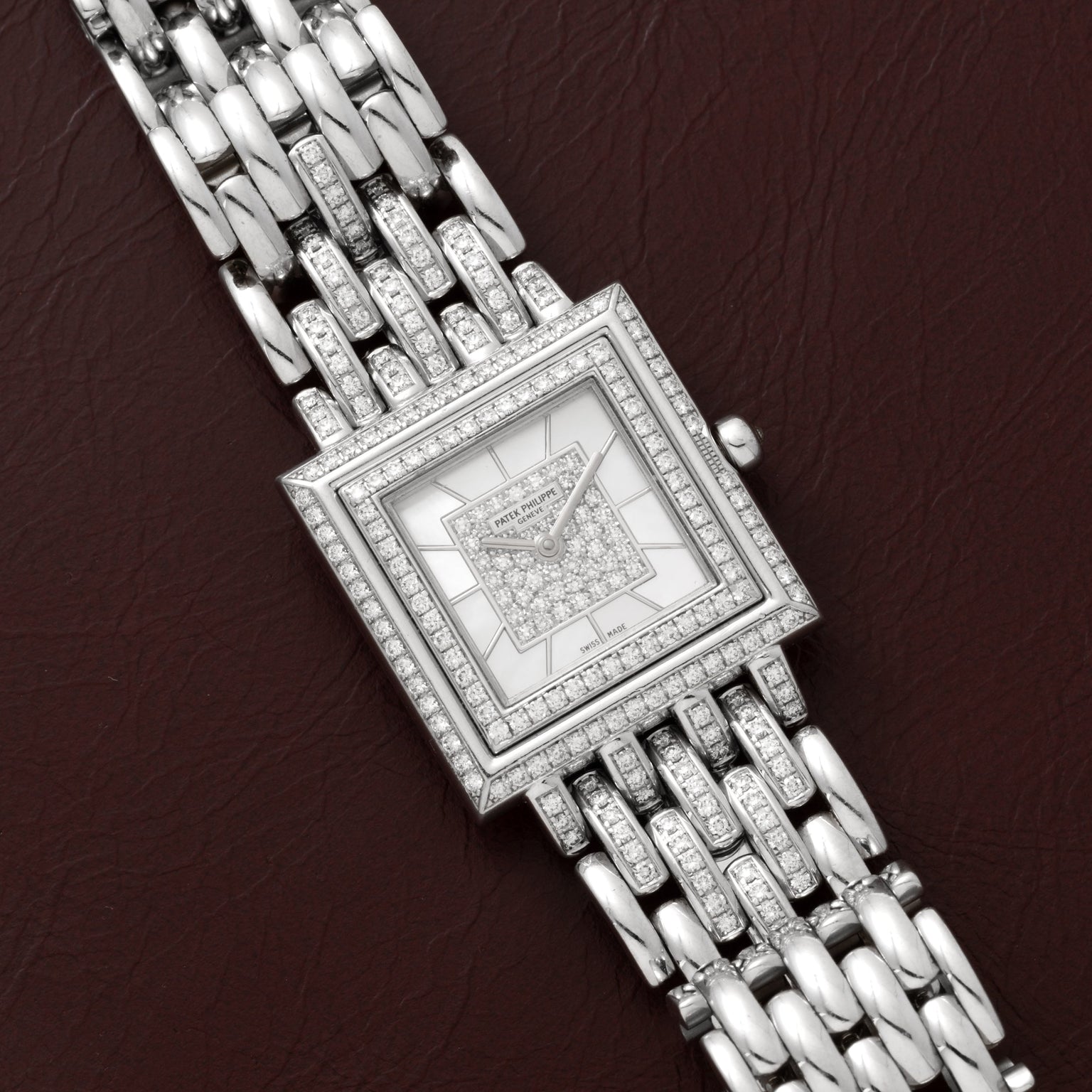Patek Philippe Gondolo square silver wristwatch with diamond accents displayed on a brown leather surface.
