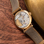 The Patek Philippe Calatrava gold wristwatch, featuring a visible intricate mechanical movement, is displayed on a wooden surface next to a brass object.