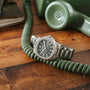 A Patek Philippe Aquanaut silver wristwatch rests on a coiled green phone cord atop a wooden table.