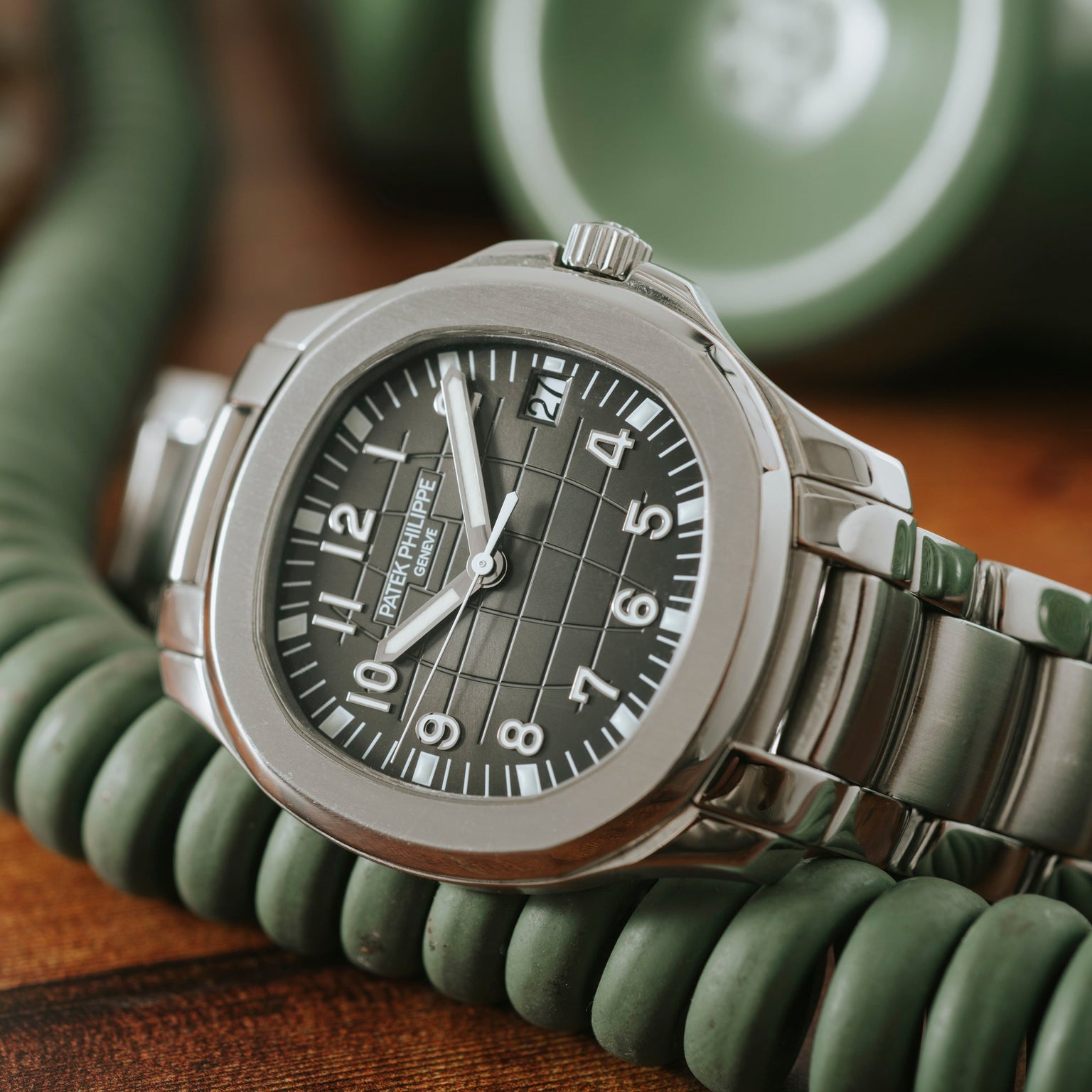The Patek Philippe Aquanaut wristwatch with a dark green dial rests on a coiled green telephone cord.