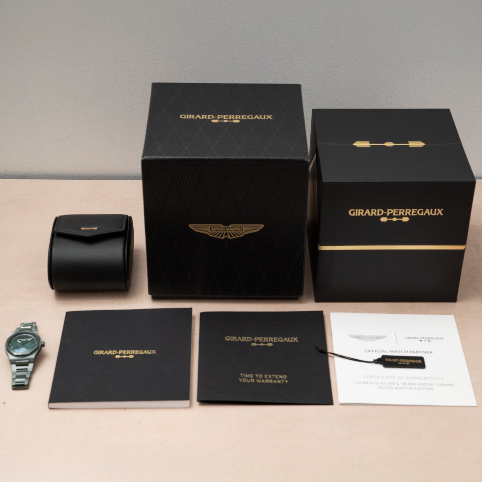 A Girard-Perregaux Laureato Green Ceramic Aston Martin Edition watch with its box, warranty card, booklet, and certificate on a table.