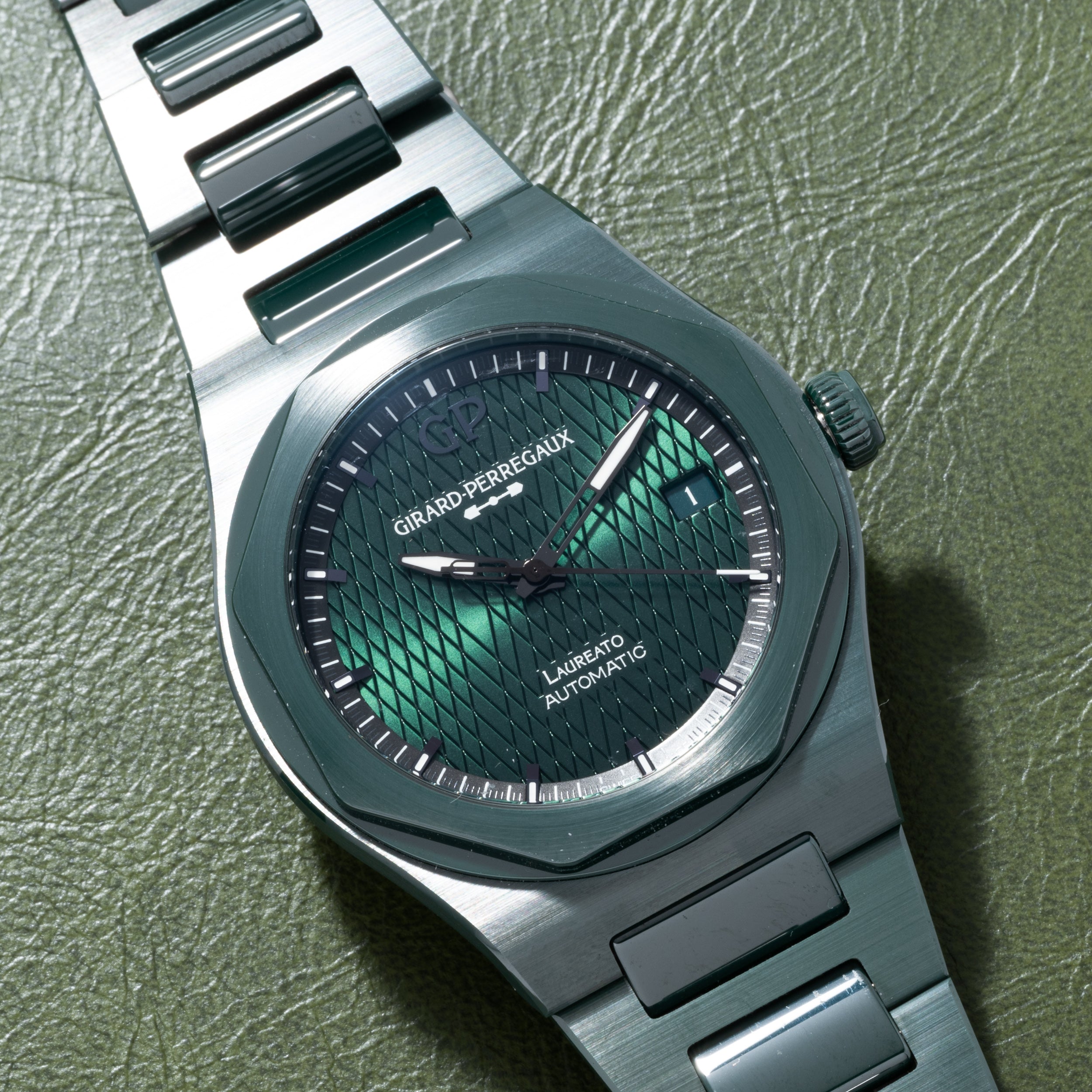 The Girard-Perregaux Laureato Green Ceramic Aston Martin Edition features a green textured dial, showcased on a green leather surface.