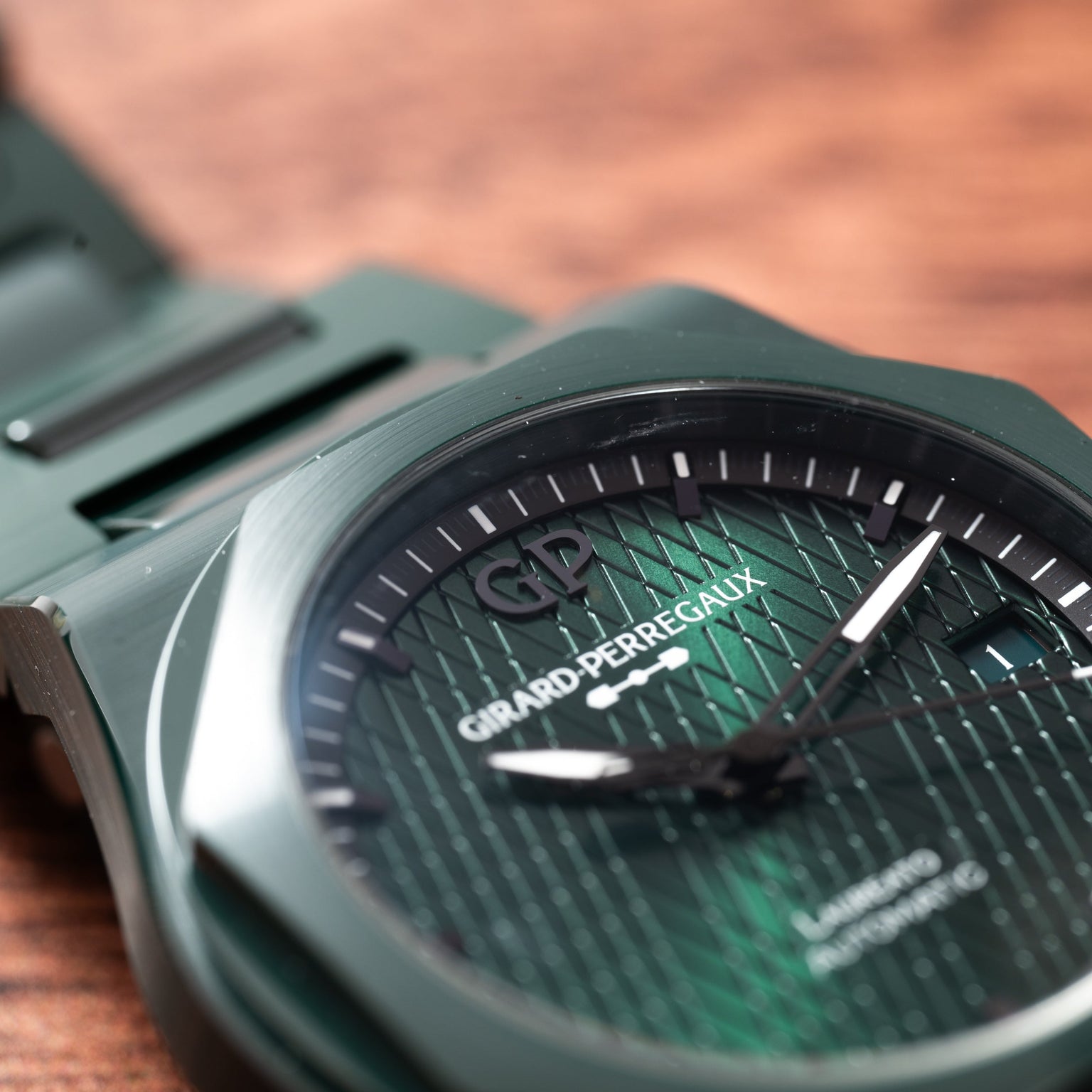 Close-up of the Laureato Green Ceramic Aston Martin Edition by Girard-Perregaux, highlighting its green dial and hands on a wooden surface.