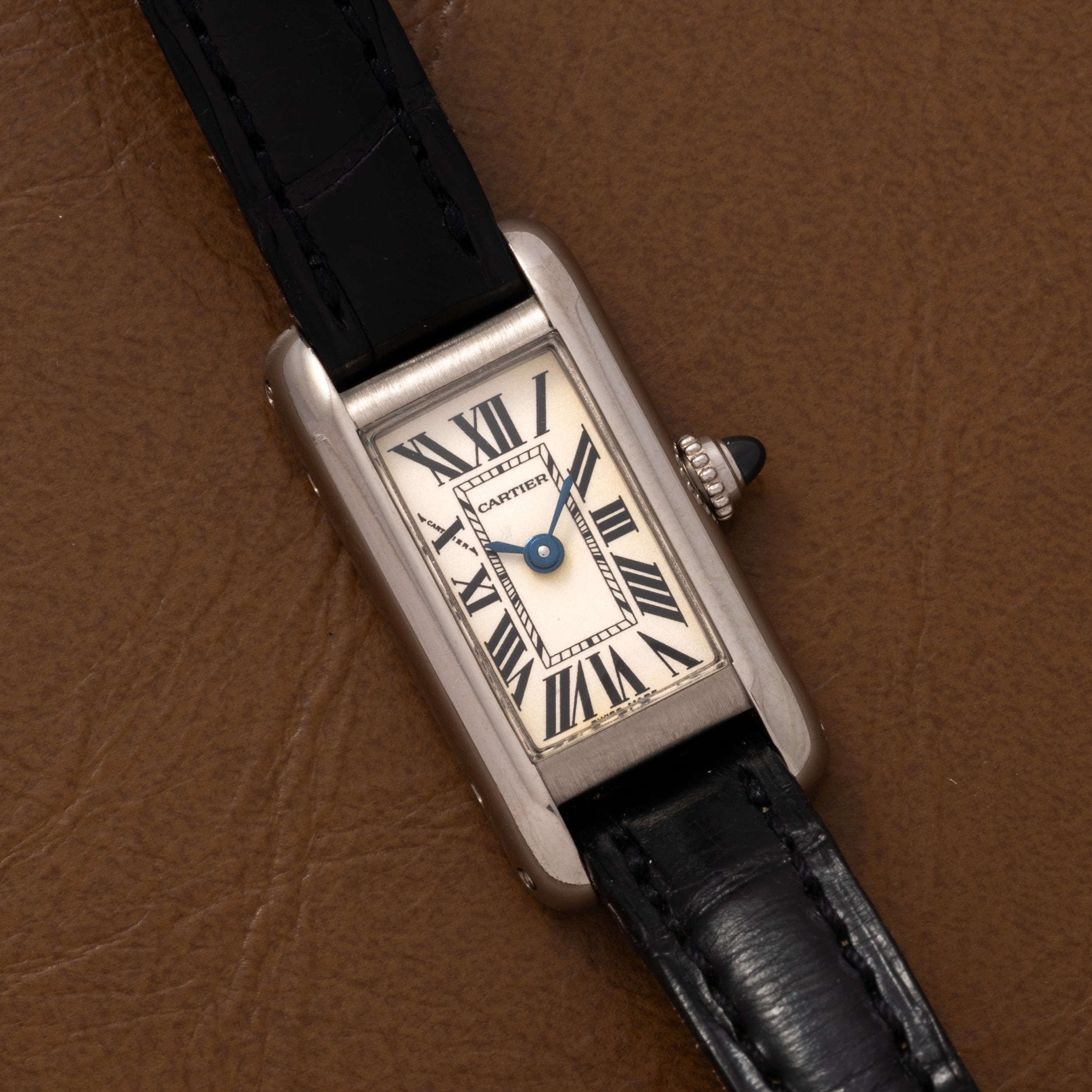A Cartier Tank Ladies Allongee wristwatch with Roman numerals and a black leather strap displayed on a brown leather surface.