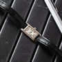 A Cartier Tank Ladies Allongee wristwatch with a black leather strap rests on a black leather surface near a silver pen.