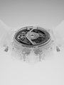Transparent watch case displaying exposed mechanical movement with gears and dial against gray background.