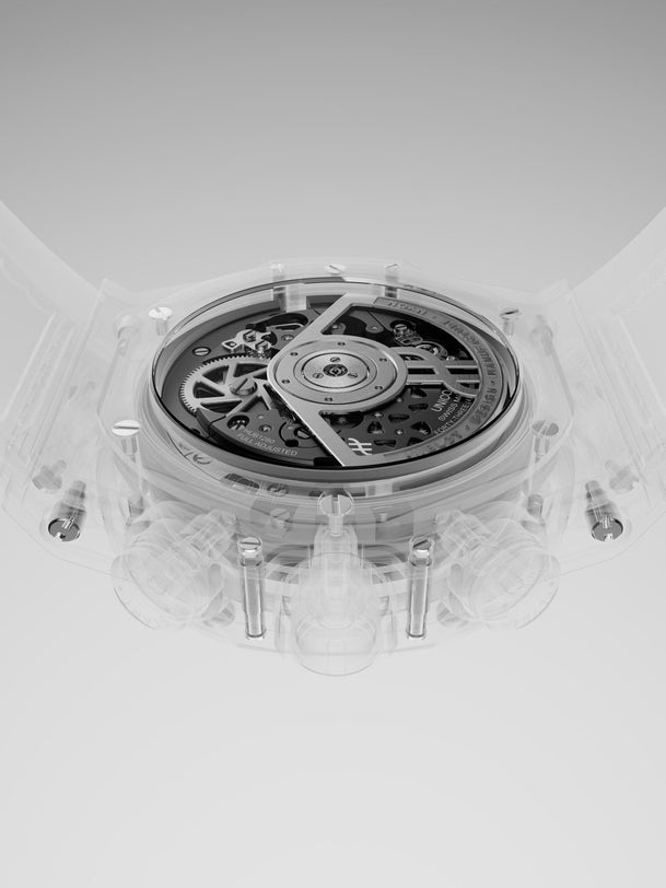 Transparent watch case displaying exposed mechanical movement with gears and dial against gray background.