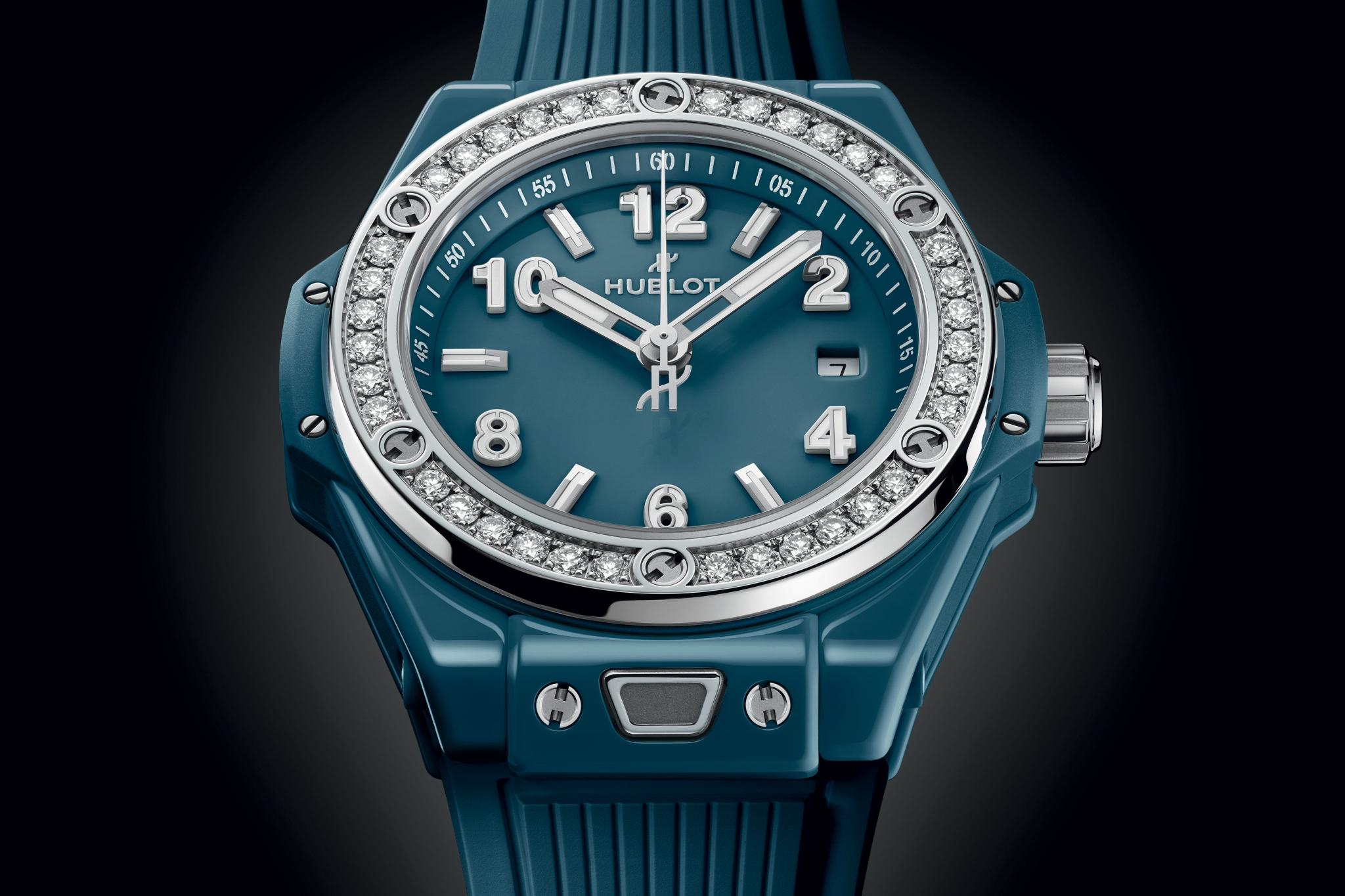 Petrol blue ceramic watch with diamond-set bezel, white numerals, and silver-tone hands.