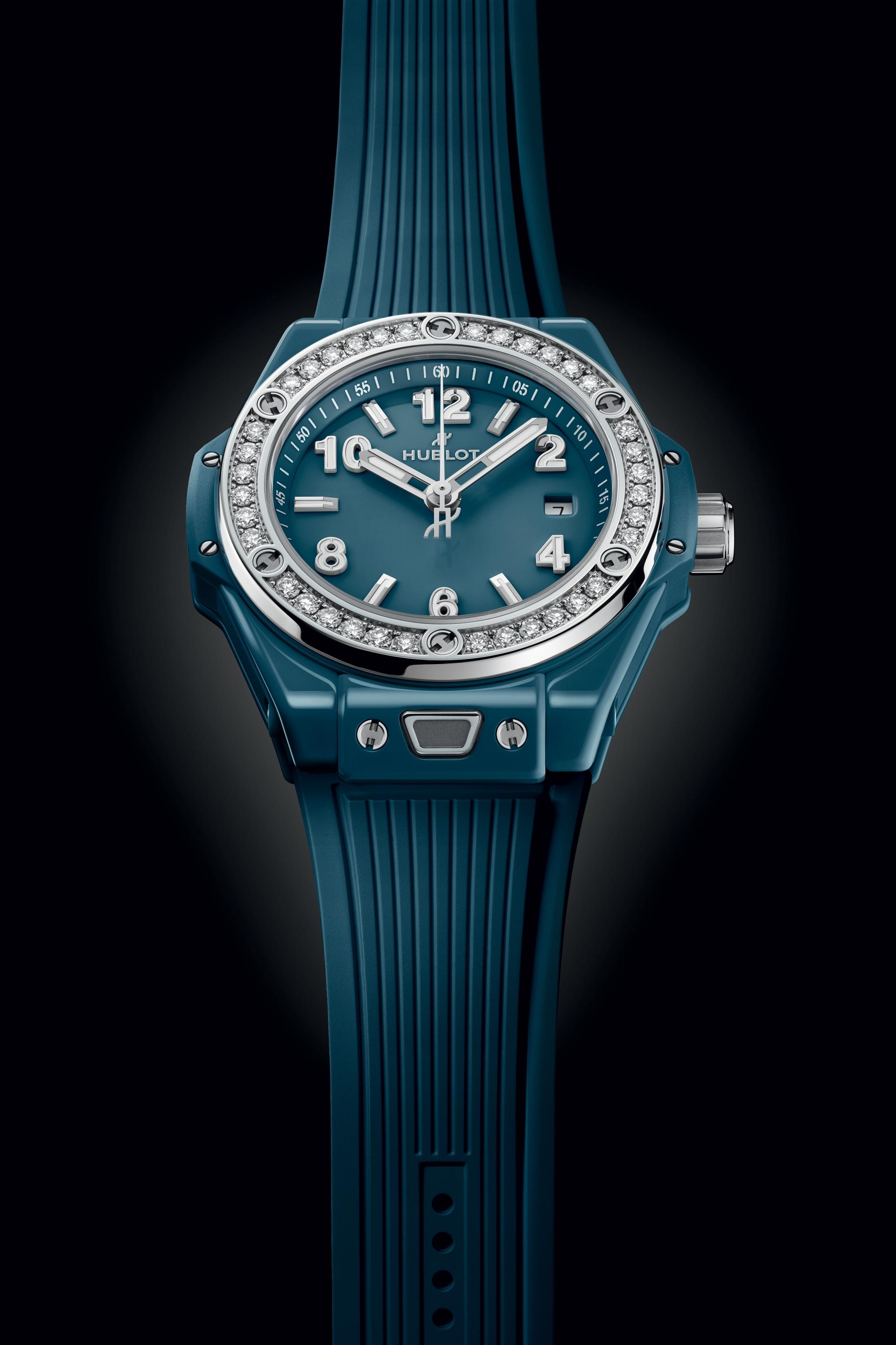 Petrol blue ceramic women's watch with diamond-set bezel, white hands and numerals on teal dial, and ribbed rubber strap.