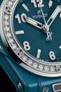 Petrol blue ceramic watch with diamond-set bezel, silver hands and numerals, Hublot branding visible on dial.