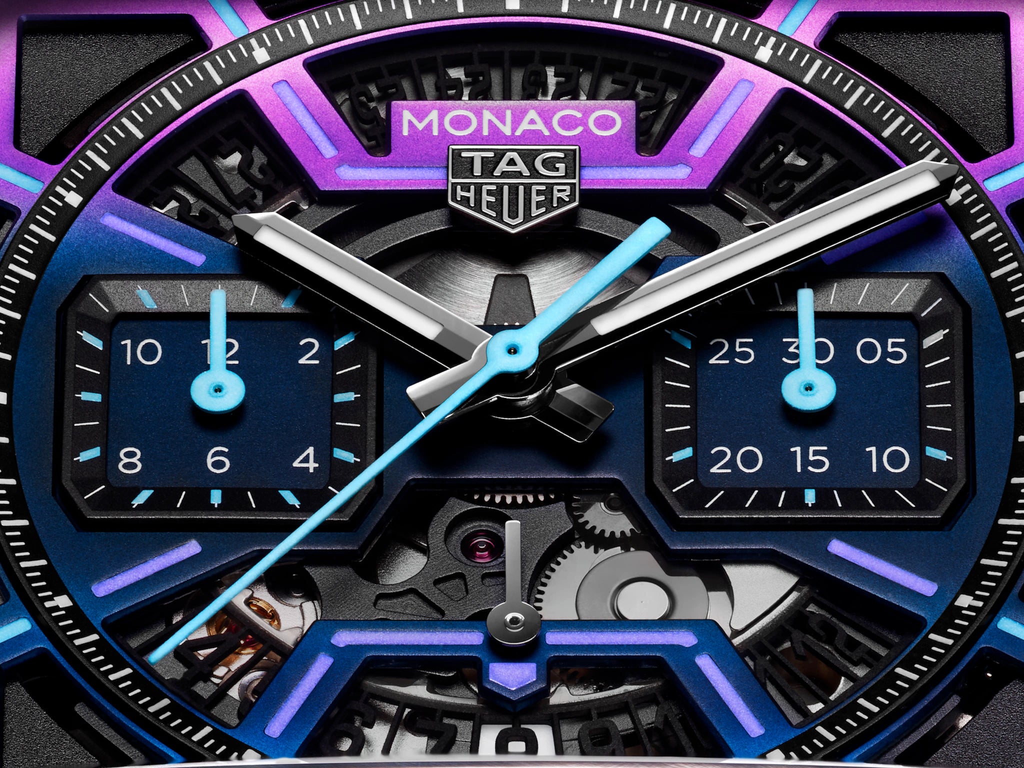 Close-up of the TAG Heuer Monaco Chronograph Las Vegas Edition watch face, featuring a geometric blue and purple design, square subdials, exposed gears, and a sleek titanium DLC-coated case. TAG Heuer logo appears at the top center.