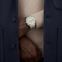Silver stainless steel chronograph watch with cream dial and subdials, worn on wrist between navy and beige jacket layers.