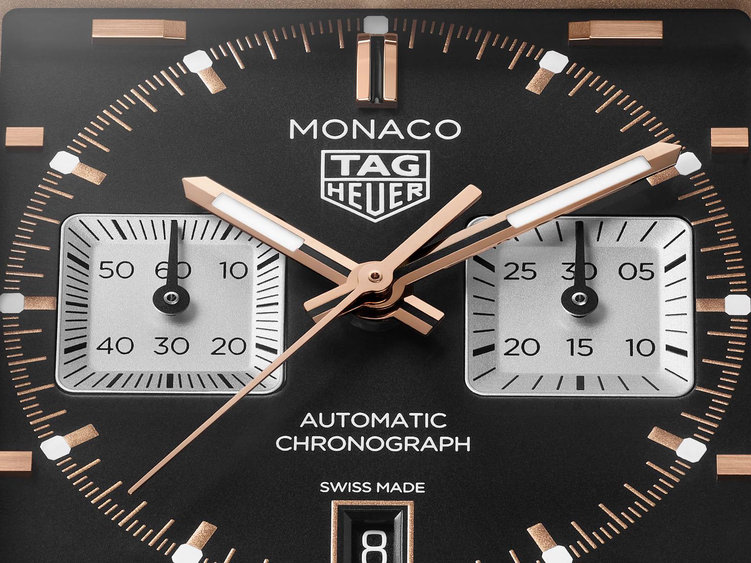 TAG Heuer Monaco chronograph watch face with black dial, rose gold hands, two square subdials, and tachymeter bezel.