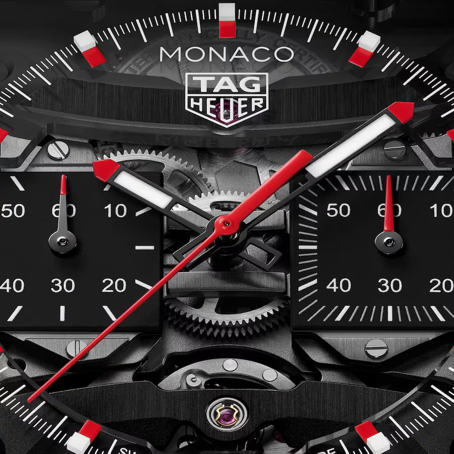 TAG Heuer Monaco Evergraph watch face with black dial, red and white hands, visible gears, and tachymeter scale.