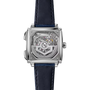 Square stainless steel watch with exposed mechanical movement visible through clear case back, dark blue leather strap.