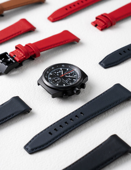 Black watch with red and black straps on a light gray surface