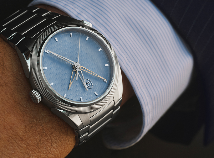 Silver watch with blue face on a wrist, wearing a light blue shirt.