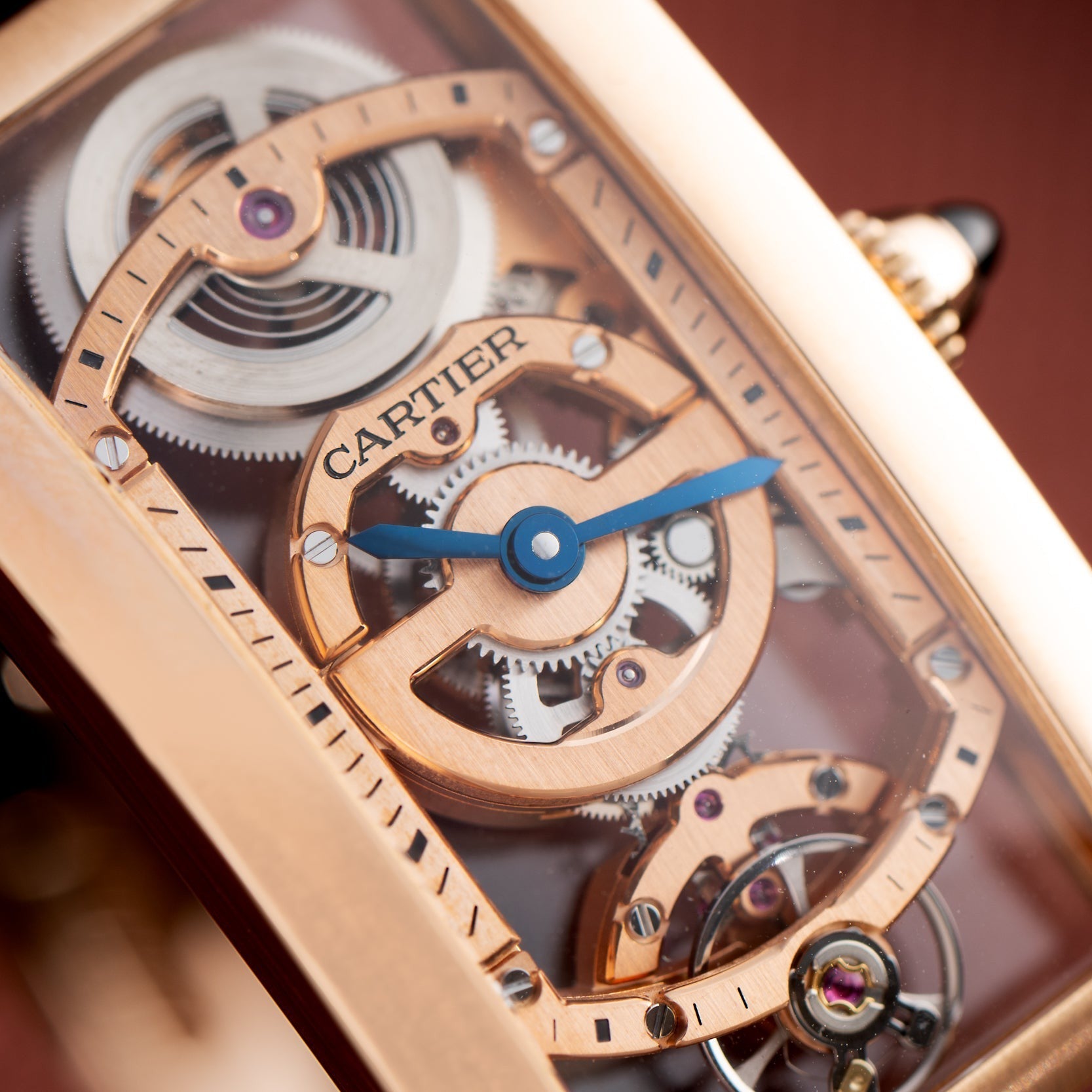 Close-up of the Cartier Tank Cintreé Skeleton watch, highlighting its exposed gears, blue hands, and gold detailing.