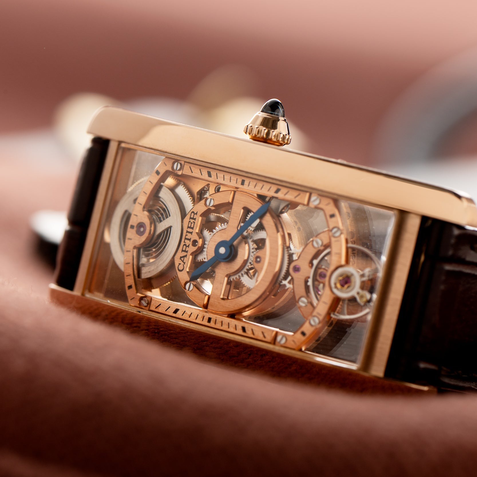 Close-up of the Cartier Tank Cintreé Skeleton watch, featuring a rectangular gold case and exposed inner mechanisms.