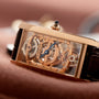 Close-up of the Cartier Tank Cintreé Skeleton watch, featuring a rectangular gold case and exposed inner mechanisms.