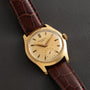 The Patek Philippe Calatrava gold wristwatch with a brown leather strap rests on a dark surface.