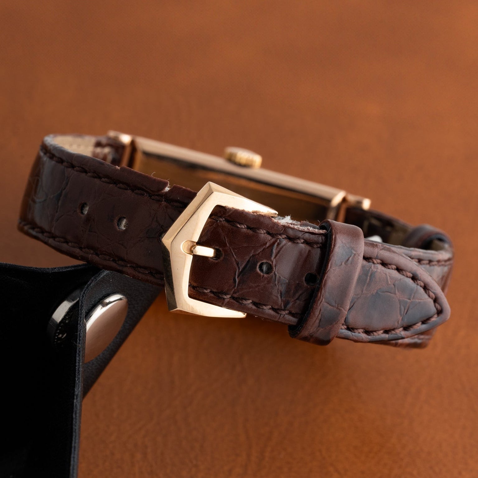 Close-up of the Patek Philippe Tegolino Dress Watch featuring a brown leather strap with a gold buckle, displayed on a brown surface.