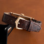 Close-up of the Patek Philippe Tegolino Dress Watch featuring a brown leather strap with a gold buckle, displayed on a brown surface.
