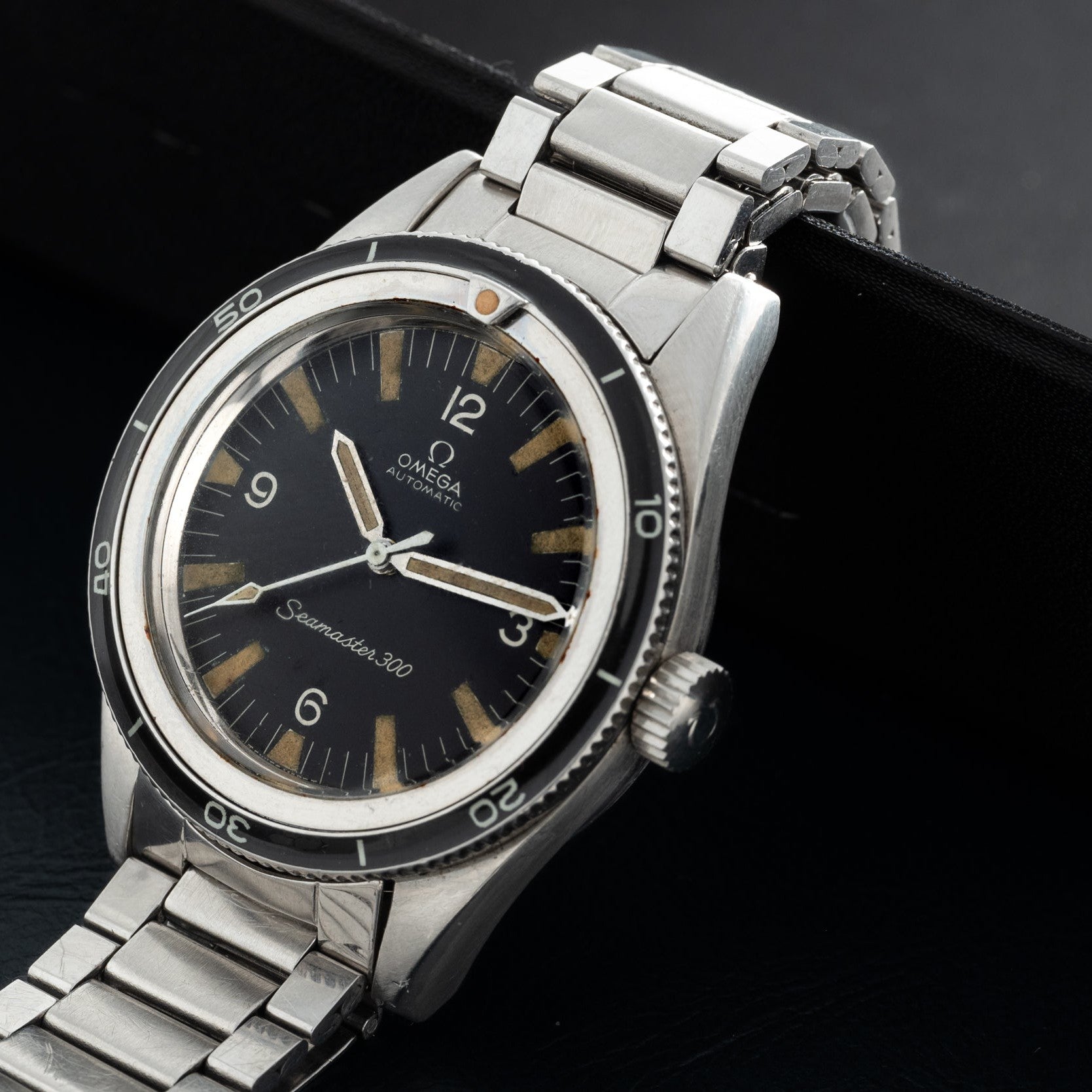 An OMEGA Seamaster 300 watch with a black dial and silver metal bracelet is displayed on a black surface.