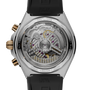 Stainless steel watch with exposed mechanical movement, gold-tone chronograph pushers, and black rubber strap.