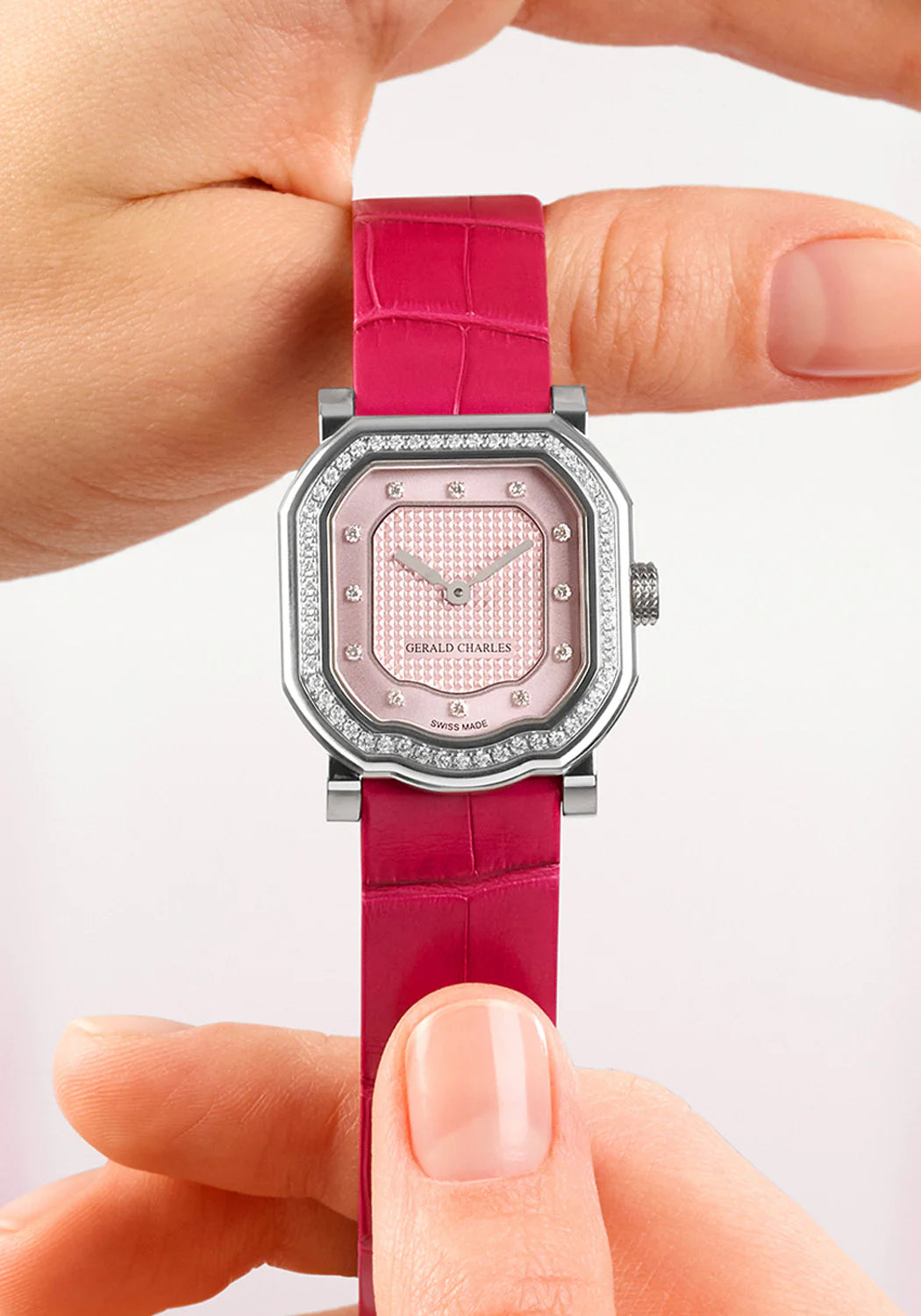 Pink watch with diamond-studded face held between fingers against a light background