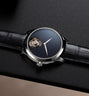 Steel watch with dark blue speckled dial, exposed tourbillon at 9 o'clock, and black leather strap.