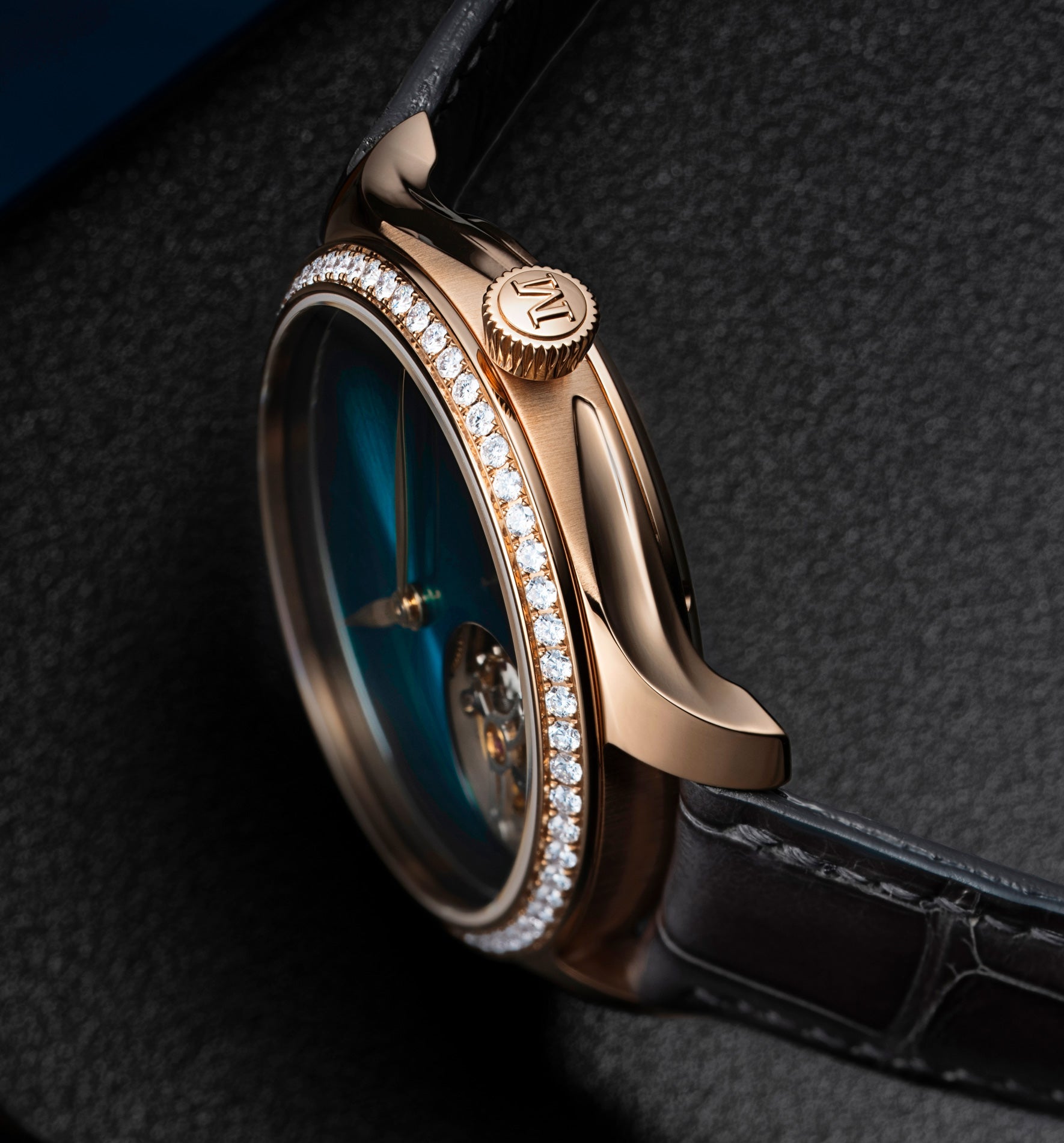 Rose gold watch with blue dial, diamond-set bezel, visible tourbillon mechanism, and black leather strap.