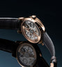 Rose gold tourbillon watch with black leather strap and visible mechanical movement through transparent case back.