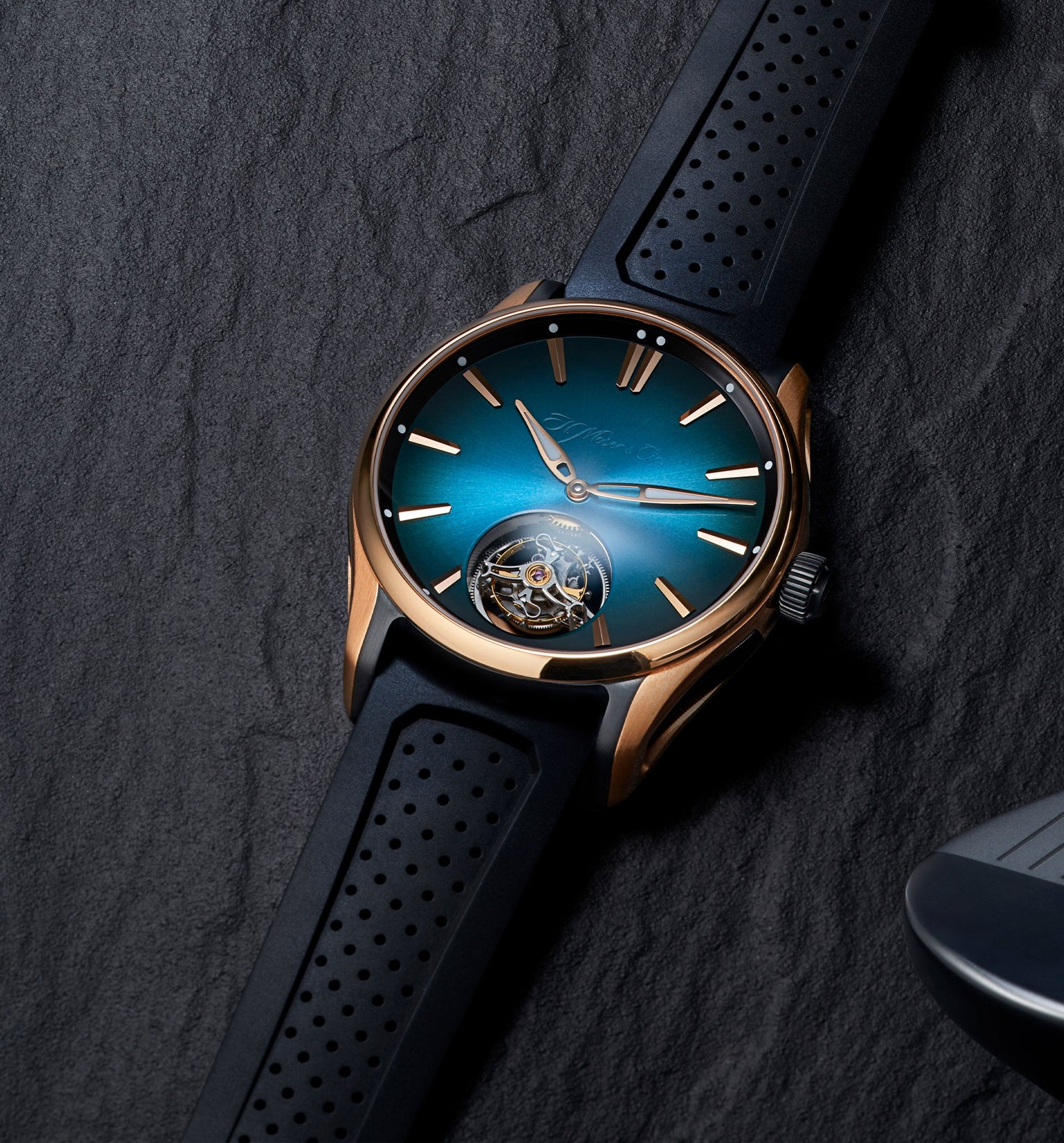 Rose gold watch with blue sunburst dial, visible tourbillon at 6 o'clock, and black perforated rubber strap.