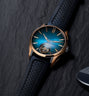 Rose gold watch with blue sunburst dial, visible tourbillon at 6 o'clock, and black perforated rubber strap.