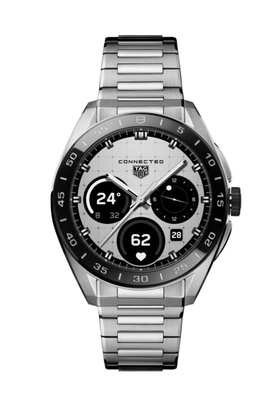 The TAG Heuer Connected Calibre E5 45mm is a silver luxury connected watch with a metal band, black ceramic bezel, and a digital dial showing time, date, temperature, heart rate, and step count in black and white.