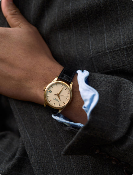Gold watch on a person's wrist with a dark suit jacket