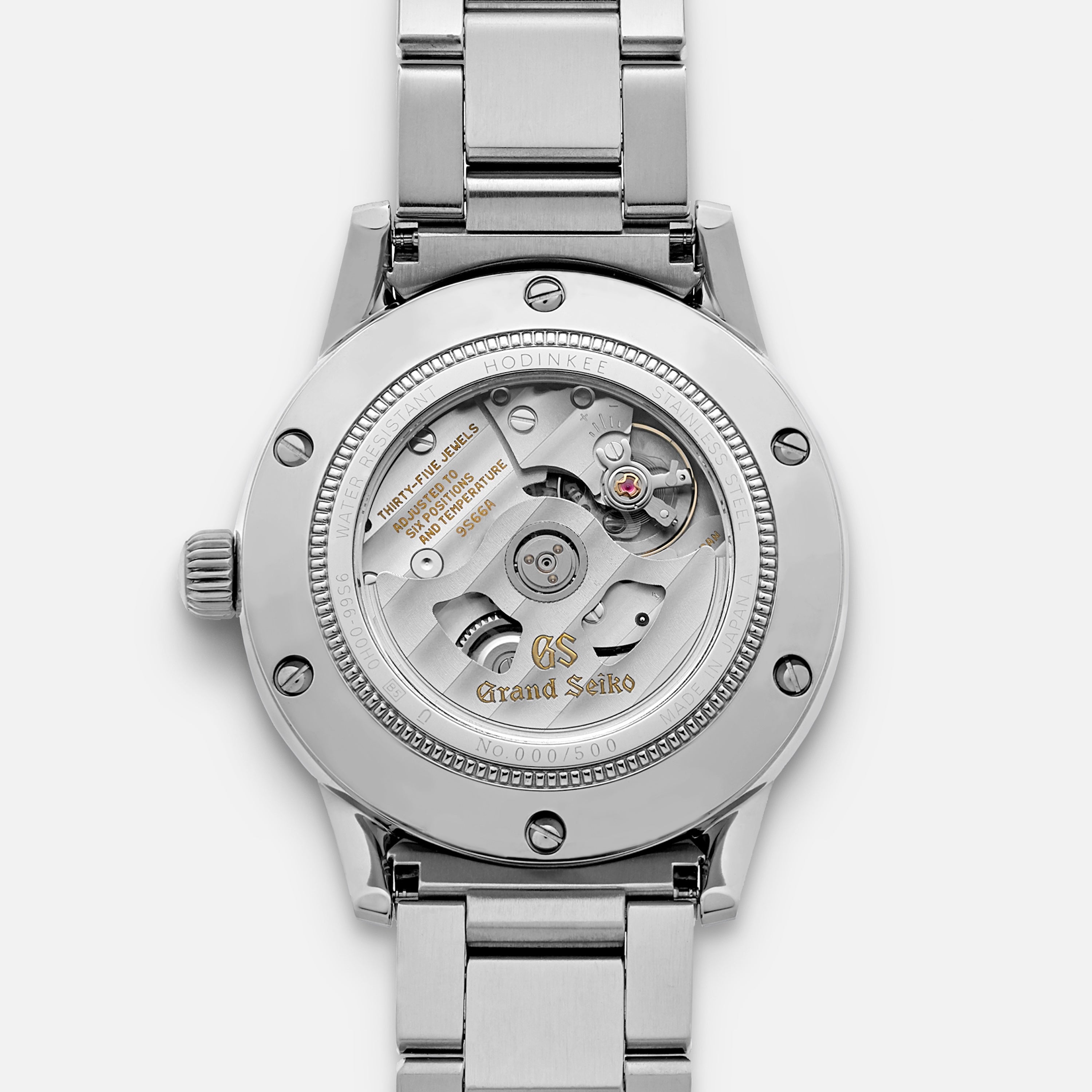 A close-up of the Grand Seiko Automatic GMT SBGM239 Limited Edition For HODINKEE highlights its open mechanical movement, engraved case back with Grand Seiko branding, unique serial number, and stainless steel bracelet.