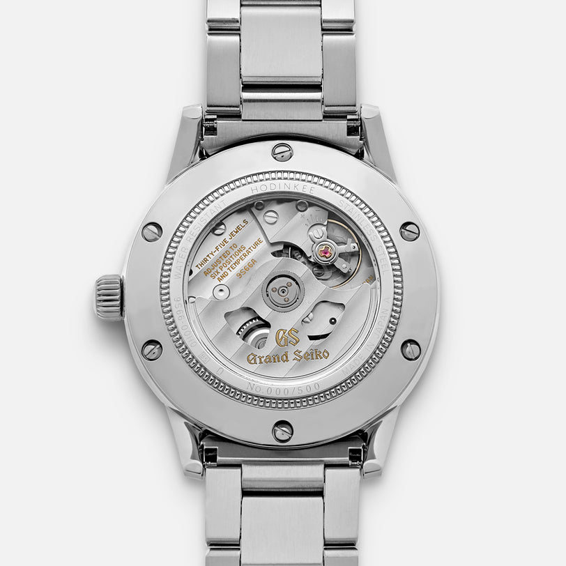 A close-up of the Grand Seiko Automatic GMT SBGM239 Limited Edition For HODINKEE highlights its open mechanical movement, engraved case back with Grand Seiko branding, unique serial number, and stainless steel bracelet.